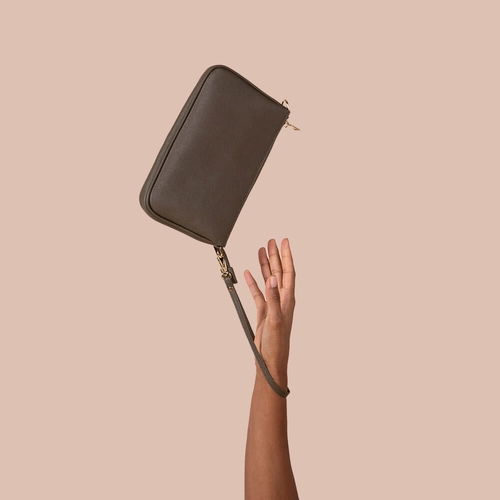 Hand holding a taupe leather wristlet against a pink backdrop