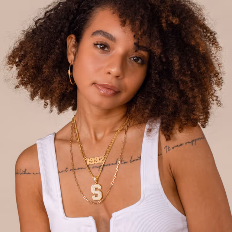 Model wearing layered gold necklaces and hoop earrings